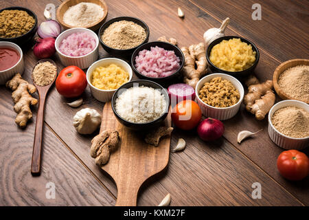 Ingwer, Knoblauch, Zwiebel und Tomatenmark und Pulver in und rohen Form. Gruppe von grundlegenden indischen Lebensmittelzutaten über Holz- Hintergrund. Selektiver Fokus Stockfoto