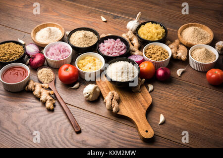 Ingwer, Knoblauch, Zwiebel und Tomatenmark und Pulver in und rohen Form. Gruppe von grundlegenden indischen Lebensmittelzutaten über Holz- Hintergrund. Selektiver Fokus Stockfoto