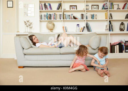 Schwangere Frau auf Sofa mit Smartphone und Töchter sitzen auf dem Boden zeichnen Stockfoto