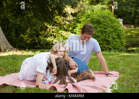 Mitte der erwachsenen Eltern mit zwei Töchtern nach vorne beugen auf Picknickdecke in Park Stockfoto
