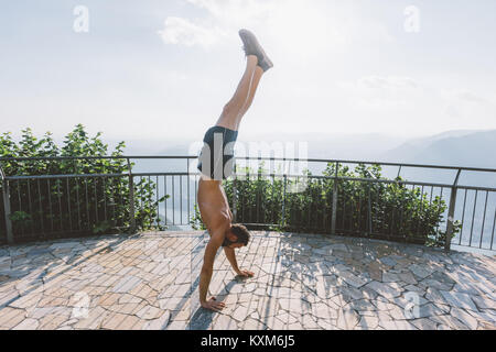 Junger Mann macht Handstand auf der Aussichtsplattform, Comer See, Lombardei, Italien Stockfoto