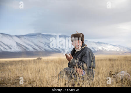 Mongolische Land ländliche alter Mann rauchen Zigarette Pelzmütze Mongolei Großvater Sitzgelegenheiten ausruhen Stockfoto