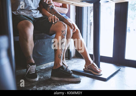 Taille abwärts von multi-ethnische hipster Paar in Cafe mit der Hand auf die Knie, Shanghai French Concession, Shanghai, China Stockfoto