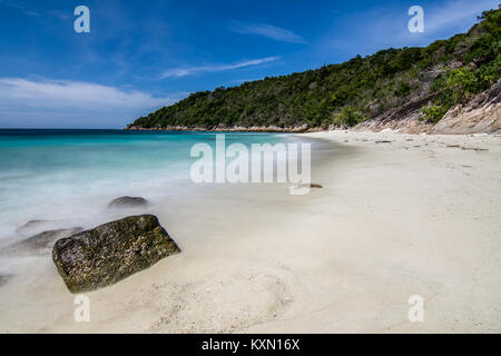 Lange Belichtung der Wellen von ruhigen Meer an tropischen weißen Sandstrand mit Tree Hill Hintergrund und blauen Himmel bedeckt. Stockfoto