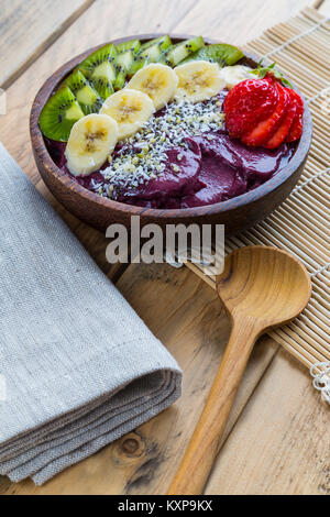 Acai Schüssel auf Holztisch - Schüssel der acai Püree mit Belag aus Banane, Kiwi, Erdbeeren und Samen. Stockfoto