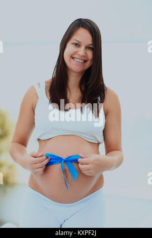 Schwangere Frau gebunden blauer Schleife auf Ihrem baby Bump. Stockfoto