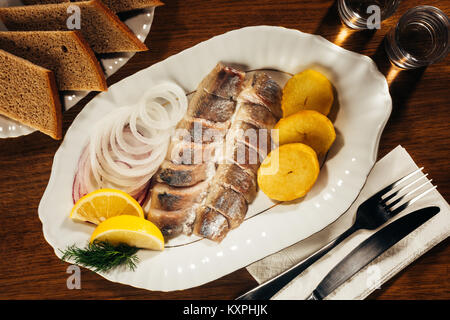 Hering fisch Schichten Festlegung auf Platte mit Zwiebel und Orangenscheiben über Tabelle mit Gabel und Messer auf Serviette und Brot Stockfoto