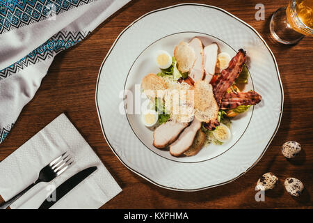 Blick auf Schinken Scheiben mit gebratenem Fleisch und einige gekochte Eier auf die Platte über der Tabelle mit Gabel und Messer auf Serviette Stockfoto