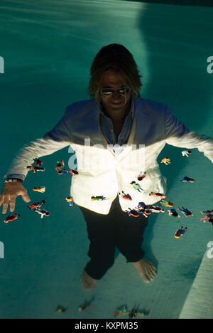 Eine elegant gekleidete Geschäftsmann mit Sonnenbrille steht unter Wasser in einen Pool von schwebenden playmobile Zahlen umgeben Stockfoto