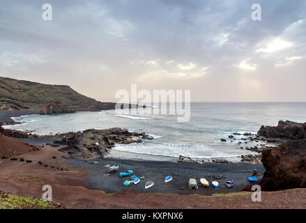 Wilden Strand am Atlantischen Ozean in El Golfo Dorf. Ein felsiger Strand mit Fischerbooten von vulkanischen Bergen umgeben Stockfoto