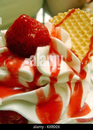 Close up Hochformat geschossen von Vanilleeis übergossen in roter Sauce mit einer Erdbeere am oberen und einem Wafer eingefügt. Stockfoto