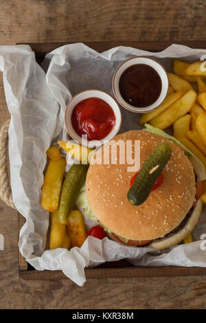 Hamburger mit Pommes Frites, Tomaten und Barbeque Sauce in Holz- Fach auf Holz rustikale Tischplatte platziert. Topview. Stockfoto