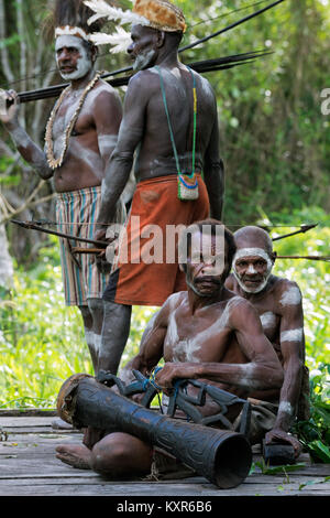 Headhunter eines Stammes von Asmat in traditioneller Kleidung und Malen mit Trommel. Stockfoto