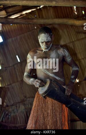 Asmat, mit einer Trommel. Mann aus dem Stamm der Asmat mit traditionellen Kinderschminken schlägt die Trommel. 23. Mai 2016 Stockfoto