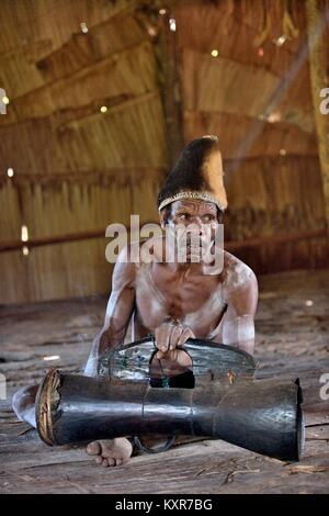 Asmat, mit einer Trommel. Mann aus dem Stamm der Asmat mit traditionellen Kinderschminken schlägt die Trommel. 23. Mai 2016 Stockfoto