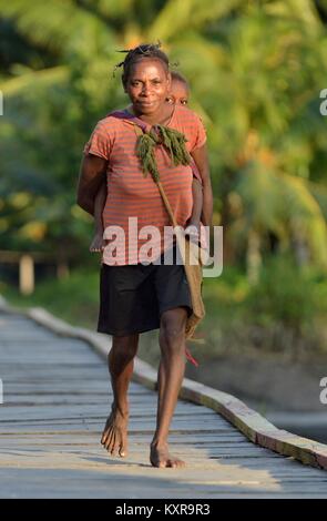 Kleines Dorf IN DEN WALD, IRIAN JAYA, Neuguinea, Indonesien - 22. MAI 2016: Portrait von nicht identifizierten Papua Frau mit Baby auf dem Rücken. Asm Stockfoto