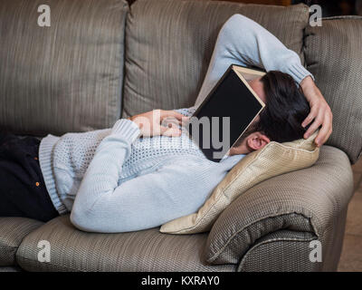 Über-arbeitete, müder junger Mann zu Hause schlafen unter Buch Stockfoto