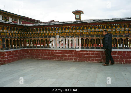 Mann truning Gebetsmühlen in der Innenstadt von Thimphu. Oben ist die Uhr der Clocktower, Bhutan Stockfoto