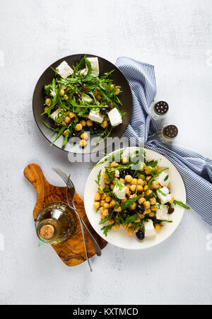 Zwei Platten von Gemüsesalat mit Kichererbsen, Rucola, Schafskäse oder Tofu und schwarzen Oliven auf dem Naturstein Hintergrund. gesunde Ernährung Stockfoto