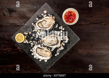 Ein Foto von frisch geöffneten Austern auf Eis mit Zitrone und traditionellen Vinaigrette Sauce, mit Kopie Raum, auf dunklen Texturen Stockfoto