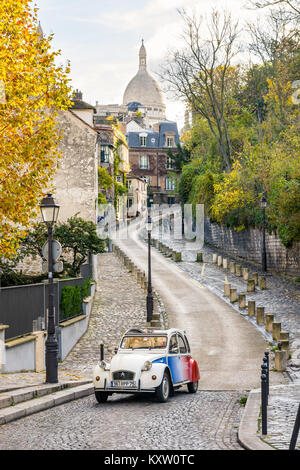 Ein französischer Oldtimer aus dem Citroën 2CV, der eine Straße von Montmartre in Paris, Frankreich, entlang fährt, mit der Basilika des Heiligen Herzens im Hintergrund. Stockfoto