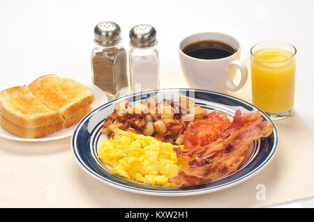 American blue Platte Frühstück mit Rührei, Hash Brown Kartoffeln, Speck, gegrillte Tomaten, Gebutterte weißen Toast, Glas Orangensaft Stockfoto