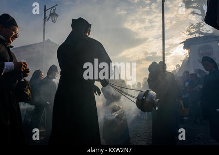 Antigua, Guatemala - 19. April 2014: Silhouette der Männer in schwarzen Roben und Hauben Räucherwerk verbreiten sich in einer Strasse der Stadt Antigua während einer pro Stockfoto