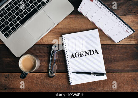 Laptop, Notebook, Gläser, Kaffee Tasse und Kalender mit Agenda Wort auf hölzernen Tisch. Tagesordnung und Zeit Management Konzept Stockfoto