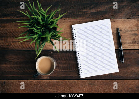Kaffee, Gläser Kugelschreiber, grüne Pflanze und leeren Notebook auf Holztisch. Flach Top View Stockfoto