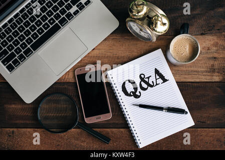 Laptop, Uhr, Telefon, Lupe, Kaffee und Notebook mit Q&A Word. Fragen und Antworten Stockfoto