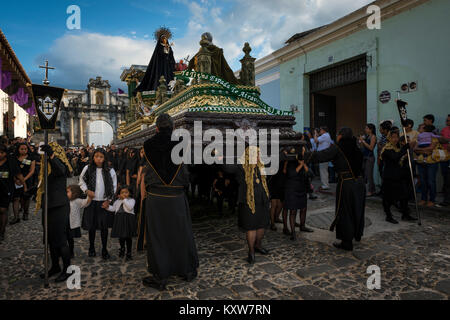 Antigua, Guatemala - 19. April 2014: Frauen in Schwarz mit einem riesigen Schwimmer in einer Straße der alten Stadt Antigua während einer Prozession der Uhr gekleidet Stockfoto