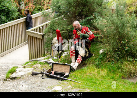 Man Straßenmusik in der schottischen Soldaten Outfit sitzend durch seine Rüstung und spielt Dudelsack am Eingang zur Klosteranlage von Glendalough Valley gekleidet Stockfoto