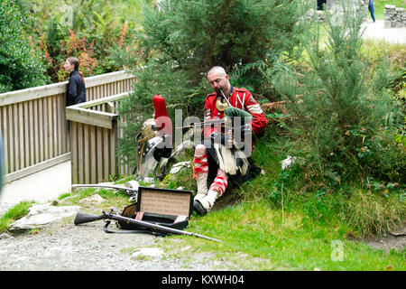 Man Straßenmusik in der schottischen Soldaten Outfit sitzend durch seine Rüstung und spielt Dudelsack am Eingang zur Klosteranlage von Glendalough Valley gekleidet Stockfoto