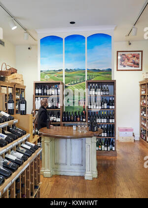 Reife oder Frau mittleren Alters Shops für Wein im Wein Shop mit Regale voll von verschiedenen Sorten von Rot- und Weißwein zum Verkauf. Stockfoto