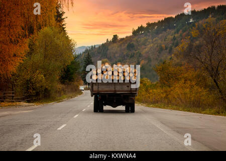 Alte Lkw voll mit Baumstämmen Reisen über bulgarische Straßen, Herbst Sonnenuntergang Stockfoto