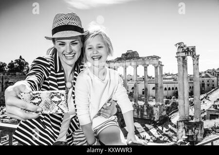 Roman Holiday. Lächeln moderne Mutter und Kind Touristen gegen Forum Romanum in Rom, Italien, mit Telefon, selfie Stockfoto