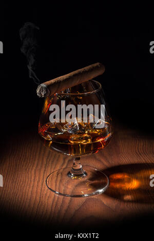 Zigarre rauchen auf ein Glas, in dem Eis und Cognac Stockfoto