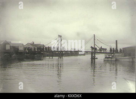 Dieses Bild aus dem frühen 20. Jahrhundert zeigt einen Trauerzug über eine Brücke über den Snake River in Nome, Alaska, und bietet einen Einblick in die Bräuche und das tägliche Leben der Zeit in der Region. Stockfoto