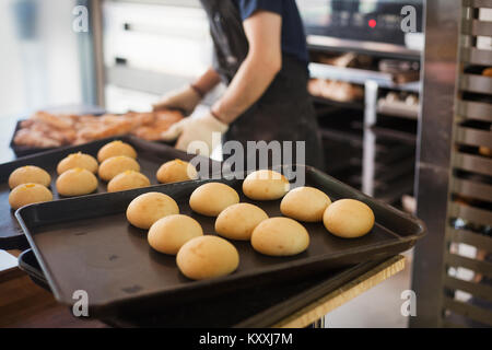 Person in einer Bäckerei arbeiten, frisch gebackene Brötchen auf großen Tabletts. Stockfoto