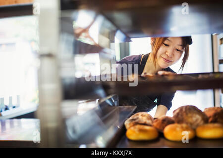 Frau in einer Bäckerei arbeiten, große Fächer mit frisch gebackenen Brötchen auf einem Trolley. Stockfoto