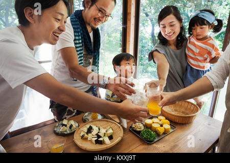 Zwei Männer, Frau mit Mädchen und Jungen gesammelt um einen Tisch mit Essen, Gläser, toasten. Stockfoto