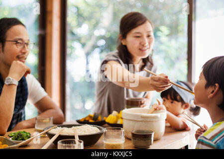 Mann, Frau und Jungen sitzen um einen Tisch mit Schüsseln mit Essen, essen. Stockfoto