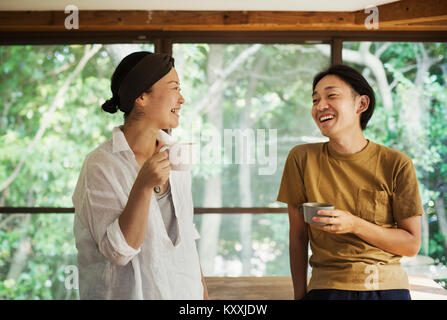 Mann und Frau stehen in Innenräumen, Kaffeetassen, lookign einander an, lächelnd. Stockfoto