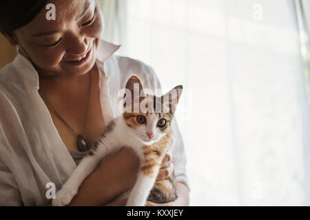 Der lächelnde Frau mit Calico Katze mit weißen, schwarzen und braunen Fell. Stockfoto