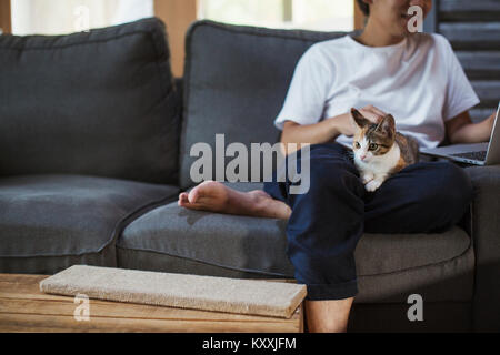 Mann sitzt auf grau , calico Katze mit weißen, schwarzen und braunen Fell auf seinem Schoß. Stockfoto