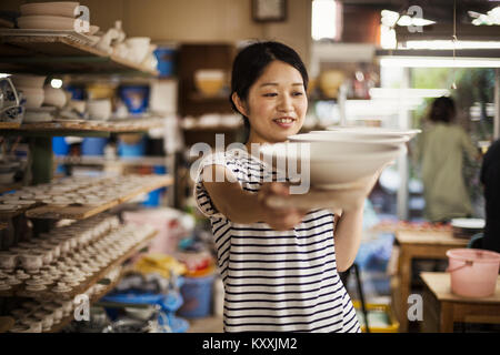 Frau, die in einer Werkstatt, die langen hölzernen Fach mit Porzellan Schalen. Stockfoto