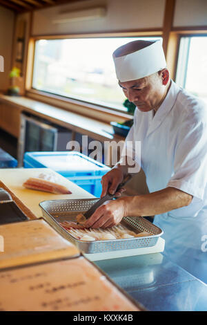 Koch arbeiten bei einem Zähler bei einer japanischen Sushi Restaurant, Fisch in Metallfach aus. Stockfoto