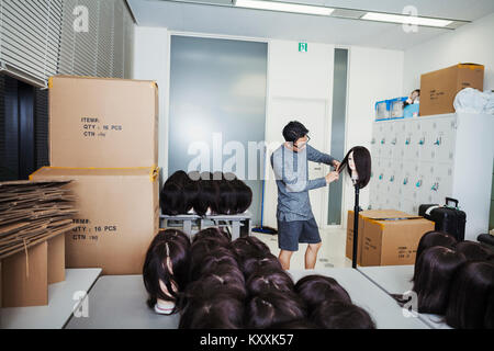 Bärtiger Mann Brille steht drinnen, Haare schneiden braune Perücke auf schaufensterpuppe Kopf. Stockfoto