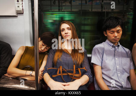 Drei Menschen, zwei Frauen und Mann, sitzen nebeneinander auf einer U-Bahn, Tokio Pendler. Stockfoto