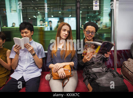 Drei Leute sitzen sidy nebeneinander auf einer U-Bahn, Lesen, Tokyo Pendler. Stockfoto